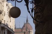 Hungary, Pest County, Budapest, Art Nouveau era apartment facades with domed roof of Hungarian Parliament Building behindand decorative metalwork and hanging spherical light in foreground.