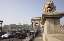 Hungary, Pest County, Budapest, lion sculpture on the Chain Bridge or Memory Bridge and passing traffic.