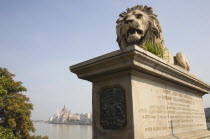 Hungary, Pest County, Budapest, lion sculpture on the Chain Bridge with Hungarian Parliament Building on far Pest bank in background.