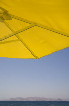 Greece, Dodecanese, Kos. Underside of bright yellow sun umbrella framing view across sea to distant coastline.   
