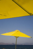 Greece, Dodecanese, Kos, bright yellow parasols on beach outside Kos Town, view towards distant coastline beyond.