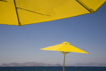 Greece, Dodecanese, Kos, bright yellow parasols on beach outside Kos Town with view towards distant coastline beyond.