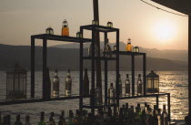 Greece, Northern Aegean, Samos, Vathy, Sun setting over water behind open air bar with the Ampelos massif beyond.