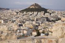 Greece, Attica, Athens, Mount Lycabettus rising in central Athens with densely populated city below part framed by wall in foreground.
