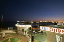 England, East Sussex, Brighton, Seafront Crazy Golf and fast food outlet on the seafront at Madeira Drive with pier illuminated at night behind.