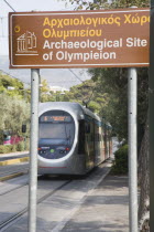 Greece, Athens, Modern tram adjacent to The Temple of Olympian Zeus with tourist heritage sign in foreground.