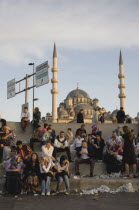 Turkey, Istanbul, Sultanahmet, Meeting place on steps in front of The New Mosque or Yeni Camii, from the Galata Bridge. Mixed crowd, many eating sitting amongst discarded rubbish with minarets and dom...