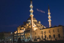 Turkey, Istanbul, Sultanahmet. The New Mosque or Yeni Camii at dusk with illuminated sign which reads Elveda meaning Go in Peace or Farewell to mark the end of Eid holiday hanging between the minarets...