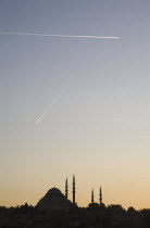 Turkey, Istanbul, Sultanahmet, Suleymaniye Mosque silhouetted against pale sunset sky with aircraft contrails high above.  