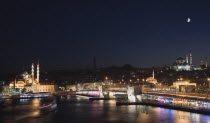 Turkey, Istanbul, Sultanahmet, The Golden Horn. The New Mosque or Yeni Camii at left, the Galata Bridge, and Suleymaniye Mosque at right illuminated at night with boats on the Bosphorus in motion blur...