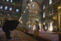 Turkey, Istanbul, Sultanahmet, The New Mosque or Yeni Camii. Tiled and highly decorated interior with elderly man worshipping, prayer performing salah or prayer.