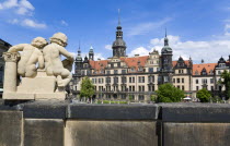 GERMANY, Saxony,Dresden, Statue of two cherubs on the Rampart of the Baroque Zwinger Palace with the Residenzschloss beyond.