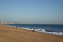 England, West Sussex, Shoreham-by-Sea, people walking along the waters edge on Shoreham beach.