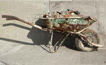 Industry, Construction, Building, Rusting wheelbarrow with a flat tyre against newly laid concrete.