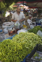 Turkey, Aydin Province, Kusadasi, Turkish stallholder selling green chilis under shade in town weekly produce market, using set of scales to weigh bag of goods.