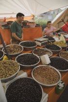 Turkey, Aydin Province, Kusadasi, Stall at weekly market  selling olives and nuts with male stall holder and young girl standing behind display and set of electronic scales.
