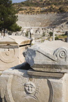 Turkey, Izmir Province, Selcuk, Ephesus, Masonry ruins with face carved in bas-relief and amphitheatre behind. 
