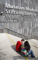 Austria, Vienna, Neubau District, Young student couple sitting on the steps of the Museum of Modern Art, Museum Moderner Kunst Stiftung Ludwig Wien or MUMOK. 
