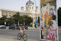 Austria, Vienna, Neubau District, Cyclist on Ringstrasse passing poster for the Leopold Museum featuring reproduction of the painting Death and Life by Gustav Klimt.