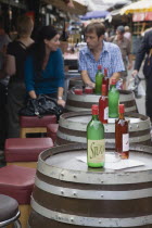 Austria, Vienna, Young couple having glass of Federweisser, wine in the fermentation stage known as Sturm in Austria seated at outside table made from a barrel. Due to the carbonic acid, Federweisser...