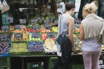 Austria, Vienna, The Naschmarkt, Two young women choosing fresh fruit from display including figs, grapes and apples outside glass shopfront.