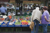 Austria, Vienna, The Naschmarkt, Customers selecting fresh fruit from display on stall that includes aubergines, mushrooms, peppers and carrots.