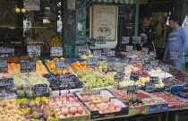 Austria, Vienna, The Naschmarkt, Owners of market fruit stall standing behind shopfront display that includes mangoes, grapes, pomegranates, mangosteens and apricots.