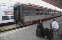 Austria, Vienna, Wien Westbahnhof, Passenger with luggage sitting on Vienna West Station with passing train. Also known as Vienna Western Station, this is a major Austrian  station and the starting po...
