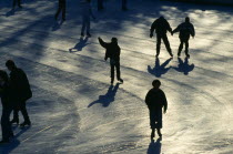 USA, New York, New York City, Manhattan, Central Park, Silhouetted ice Skaters casting long shadows.