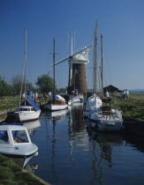 England; The Norfolk Broads, people walking along path next to canal with pleasure boats moored.