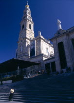 Portugal, Beira Litoral, Fatima, Woman in large hat sat at the bottom of the steps in front of the church.