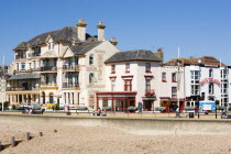 England, West Sussex, Bognor Regis, The Royal Hotel Bar and Restaurant and other buildings on the Esplanade with people walking on the promenade behind the sea wall defences on the pebble shingle beac...