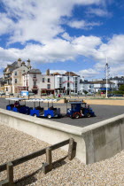 England, West Sussex, Bognor Regis, The Chugger road Train on the Esplanade with sightseeing tourists turning by the pier behind the concrete sea wall defences beyond the pebble shingle beach.