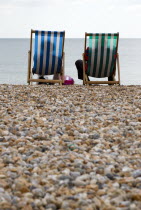 England, West Sussex, Bognor Regis, Two elderly seniors sitting on deck chairs on the pebble shingle beach looking out to sea.