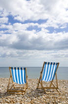 England, West Sussex, Bognor Regis, Two blue and white deck chair on the shingle pebble beach looking out to sea.