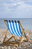 England, West Sussex, Bognor Regis, Single blue and white deck chair on the shingle pebble beach looking out to sea.