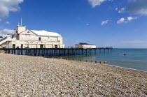 England, West Sussex, Bognor Regis, The Pier with people fishing off the end and the shingle pebble beach with people in canoes passing the pier in calm sea.