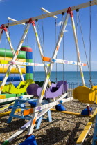 England, West Sussex, Bognor Regis, Colourful amusement swings on the pebble shingle beach by the promenade.