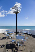 England, West Sussex, Bognor Regis, Millennium Beacon on the seafront beside the beach with empty metal tables and chairs below it on the promenade.