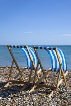 England, West Sussex, Bognor Regis, Two blue and white deck chair on the shingle pebble beach looking out to sea.