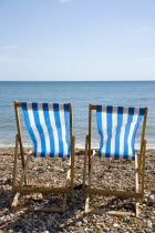 England, West Sussex, Bognor Regis, Two blue and white deck chair on the shingle pebble beach looking out to sea.