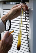 Climate, Weather, Measurements, Weather observer using a magnifying glass to read the a thermometer that records underground temperature at the Bognor Regis weather station.