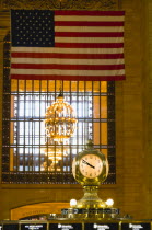 USA, New York, Manhattan, Grand Central Terminus railway station with the four faced clock above the travel information booth in the Main Concourse beneath a chandelier and the American Stars and Stri...