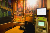 USA, New York, Manhattan, Man asleep at table beneath wall painting of Manhattan beside an ATM cash machine in Mcdonalds restaurant in Times Square.