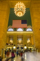 USA, New York, Manhattan, Grand Central Terminal railway station entrance to the Main Concourse from the Vanderbilt Hall with people walking below the American Stars and Stripes flag and chandelier ha...
