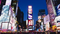 USA, New York, Manhattan, People walking at night in Times Square at the junction of 7th Avenue and Broadway below buildings with advertising on large video screens.