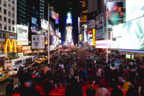 USA, New York, Manhattan, People sitting on lit red steps or walking at night in Times Square at the junction of 7th Avenue and Broadway below buildings with advertising on large video screens.