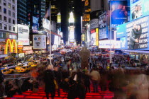 USA, New York, Manhattan, People sitting on lit red steps or walking at night in Times Square at the junction of 7th Avenue and Broadway below buildings with advertising on large video screens.