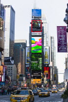 USA, New York, Manhattan, People walking in Times Square at the junction of 7th Avenue and Broadway below buildings with advertising on large video screens with yellow taxi cabs driving down 7th Avenu...