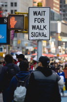 USA, New York, Manhattan, People in Times Square by pedestrian crossing sign with a red hand illuminated to stop and do not cross beside a sign that says Wait For Walk Signal.